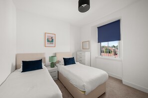 A bedroom with two beds, a window with a view, a bedside table with a lamp, and a framed picture on the wall. - Bright 2‑Bedroom St Andrews Apartment on Pipeland Road with Balcony, Views & Walk to To (St. Andrews)