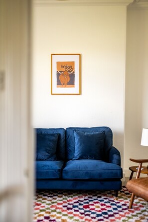 Una habitación con un sofá azul, un cuadro en la pared y una alfombra estampada.