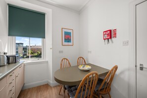 A small kitchen with a dining table, chairs, and a window with a roller blind. - Bright 2‑Bedroom St Andrews Apartment on Pipeland Road with Balcony, Views & Walk to To (St. Andrews)