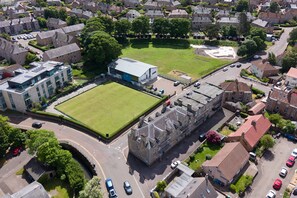An aerial view of a residential area with a large building, a green field, and a parking lot. - Bright 2‑Bedroom St Andrews Apartment on Pipeland Road with Balcony, Views & Walk to To (St. Andrews)