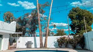 Una piscina con due palme, un edificio bianco e luci decorative su uno sfondo celeste.