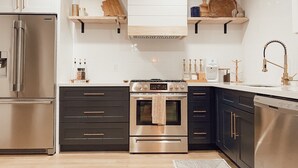 Una cucina moderna con elettrodomestici in acciaio inox, mobili in bianco e nero ed elementi a scaffale in legno.