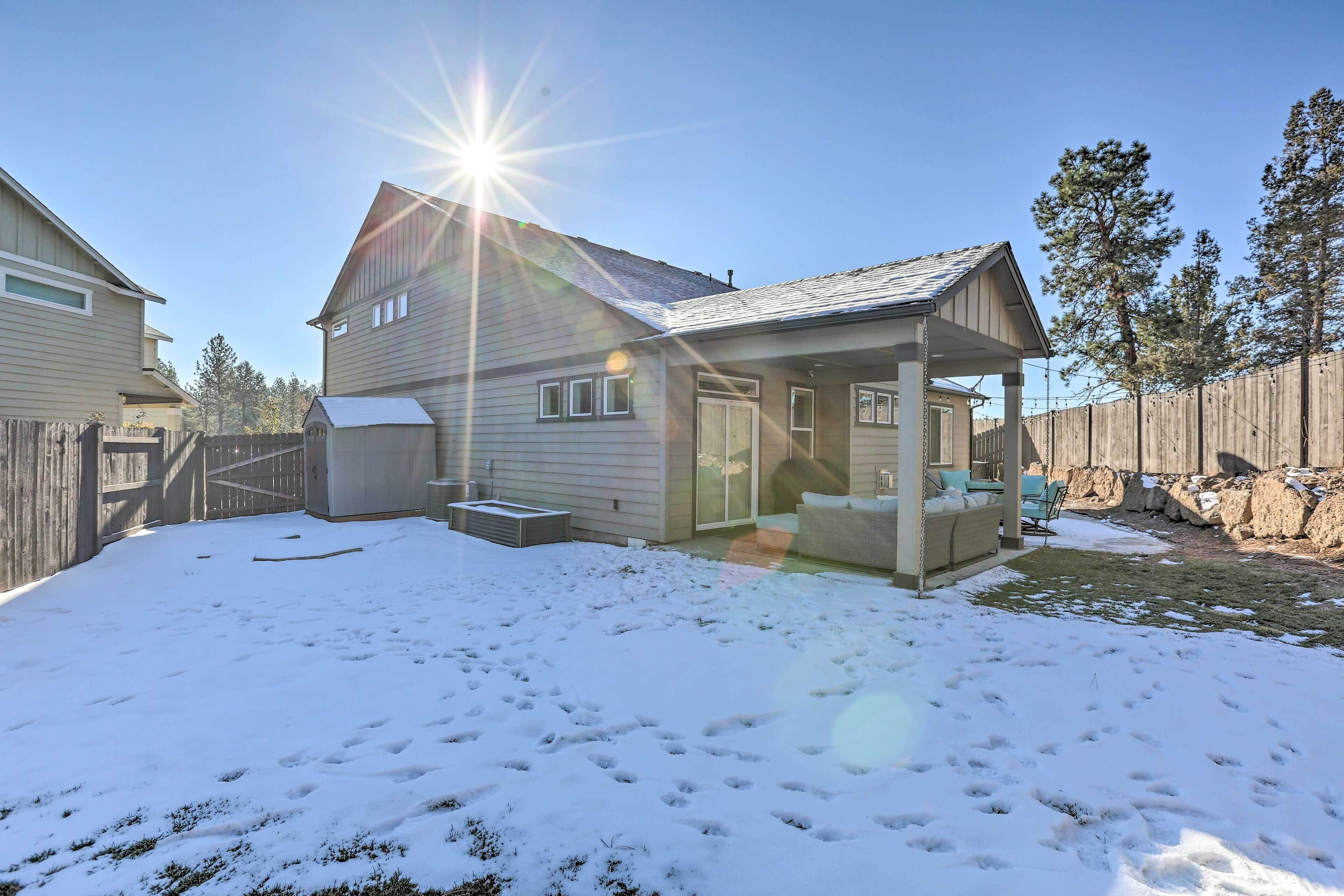 A house with a covered patio, a fenced yard, and a snow-covered ground.