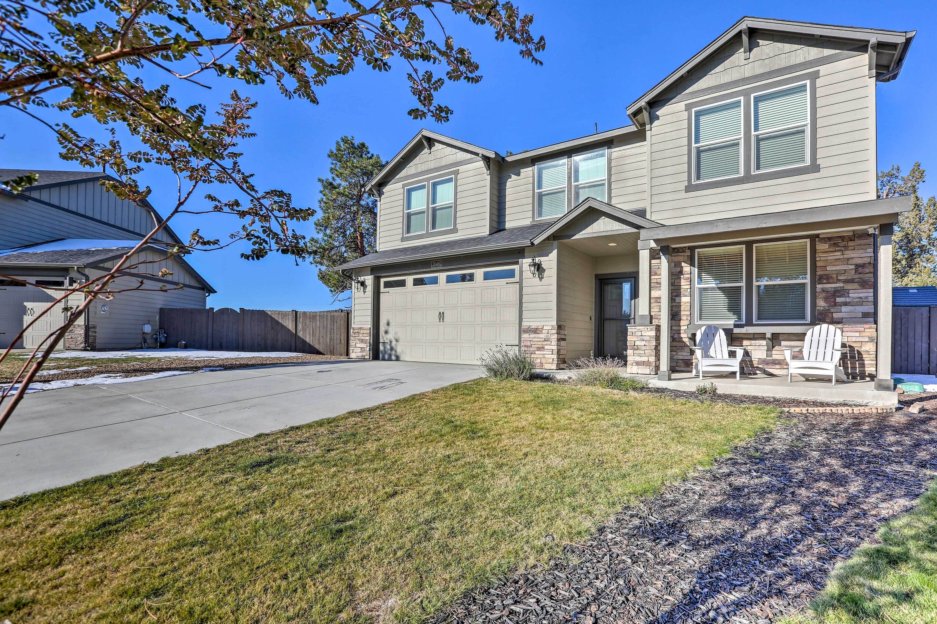 A two-story house with a garage, a covered porch with Adirondack chairs, and a well-maintained lawn.