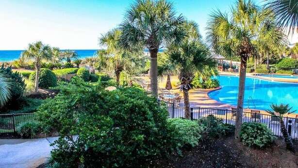 A pool area with palm trees and a view of the ocean. - Beautiful Owner Managed Condo at the Crescent - Best Complex in Destin (Miramar Beach)
