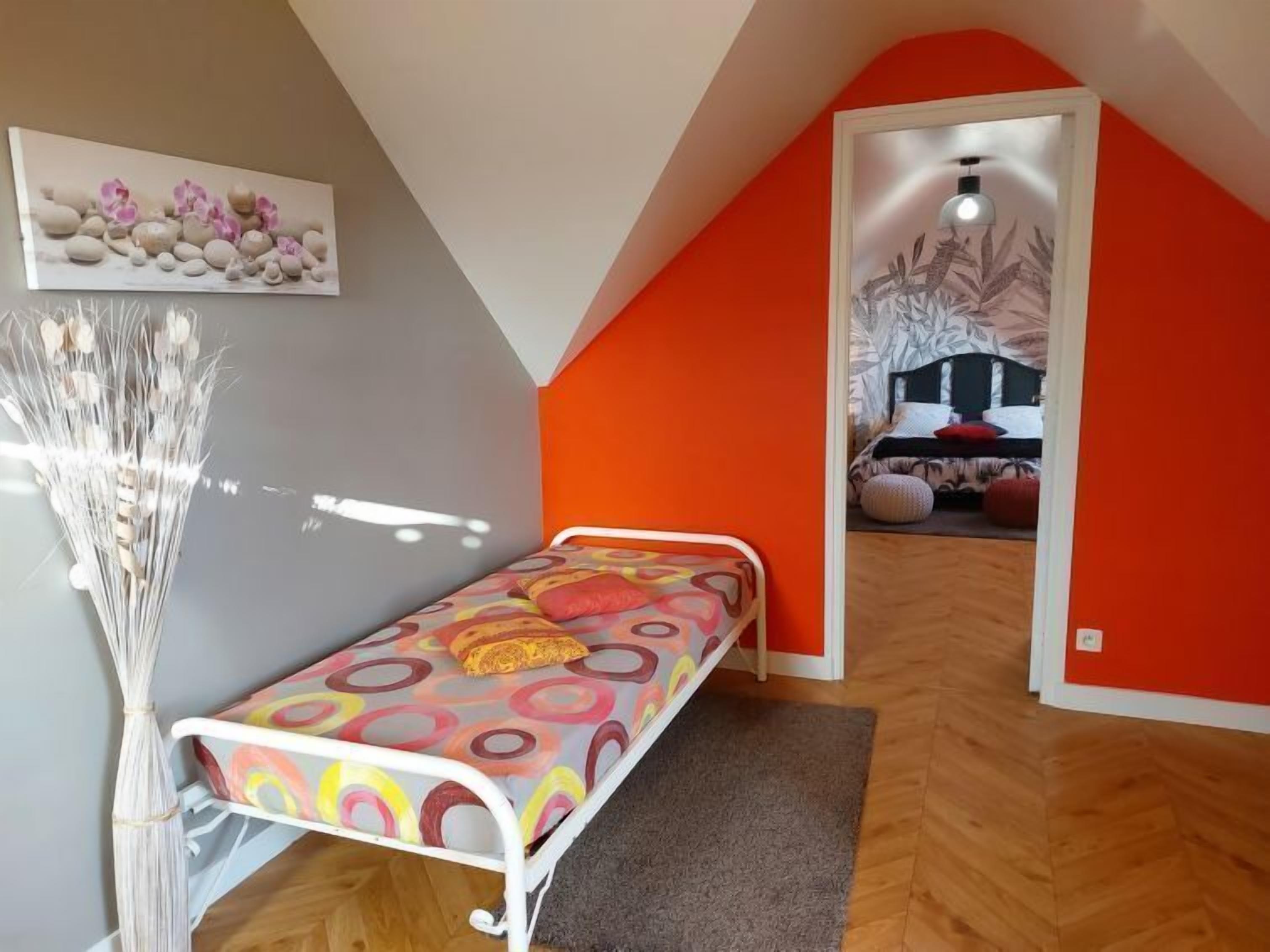Una habitación pequeña y colorida con una cama, un jarrón de flores secas y un cuadro en la pared.