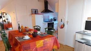 Een eetgedeelte met een tafel voor vier personen, een keuken op de achtergrond en een televisie op een kast.