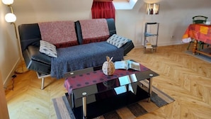 Een gezellig loft appartement met een zwarte leren bank, een glazen salontafel en een eethoek met een tafel en stoelen.