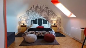 Een slaapkamer met een schuine balklaag, een bed met een hoofdeinde met bladmotief, twee nachtkastjes met lampen, en een dakraam.