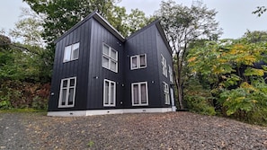 A two-story building with a dark exterior, multiple windows, and a gravel driveway.