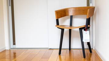 A wooden chair with a black frame and a white tag, positioned in a room with wooden flooring and white walls.