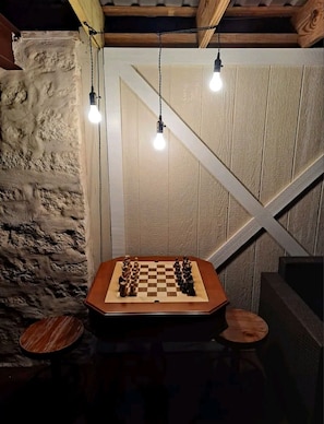 A wooden chessboard set on a table in a rustic room with exposed wooden beams and a stone wall.