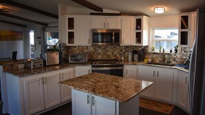 A kitchen with white cabinets, a granite countertop, stainless steel appliances, and a window with a view.