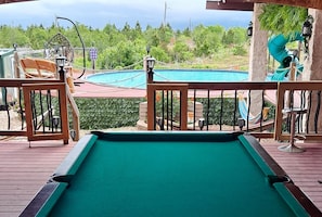 A pool table on a wooden deck with a view of a swimming pool and a slide.