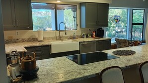 A kitchen with granite countertops, a black induction cooktop, a coffee maker, and a window with a view of greenery.