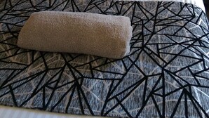 Een netjes opgemaakt bed met een beddengoed met een patroon, een kussen en een opgerolde handdoek.