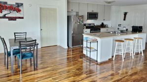 Una cucina moderna con mobili bianchi, un frigorifero in acciaio inossidabile, un forno a microonde e un piano cottura. C'è un tavolo da pranzo con sedie e una piccola isola con sgabelli.