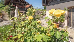 A rustic building with a balcony and a garden with yellow roses. - Maisonette apartment for 4 people, 95 sqm with terrace (Obing)