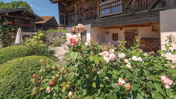 A traditional wooden chalet with a balcony, surrounded by lush greenery and blooming flowers. - Maisonette apartment for 4 people, 95 sqm with terrace (Obing)