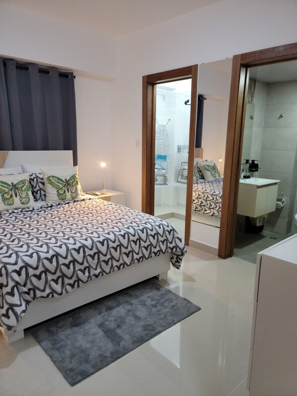 A bedroom with a bed, bedside tables, a mirror, and a bathroom visible through an open door.