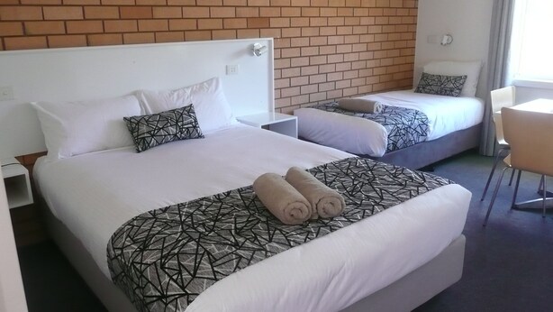 Een hotelkamer met twee bedden, elk voorzien van beddengoed en kussens met een patroon. In de kamer staat een klein tafeltje en een stoel.