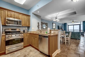 Una cocina con armarios de madera, electrodomésticos de acero inoxidable, lavavajillas y un comedor con mesa y sillas.