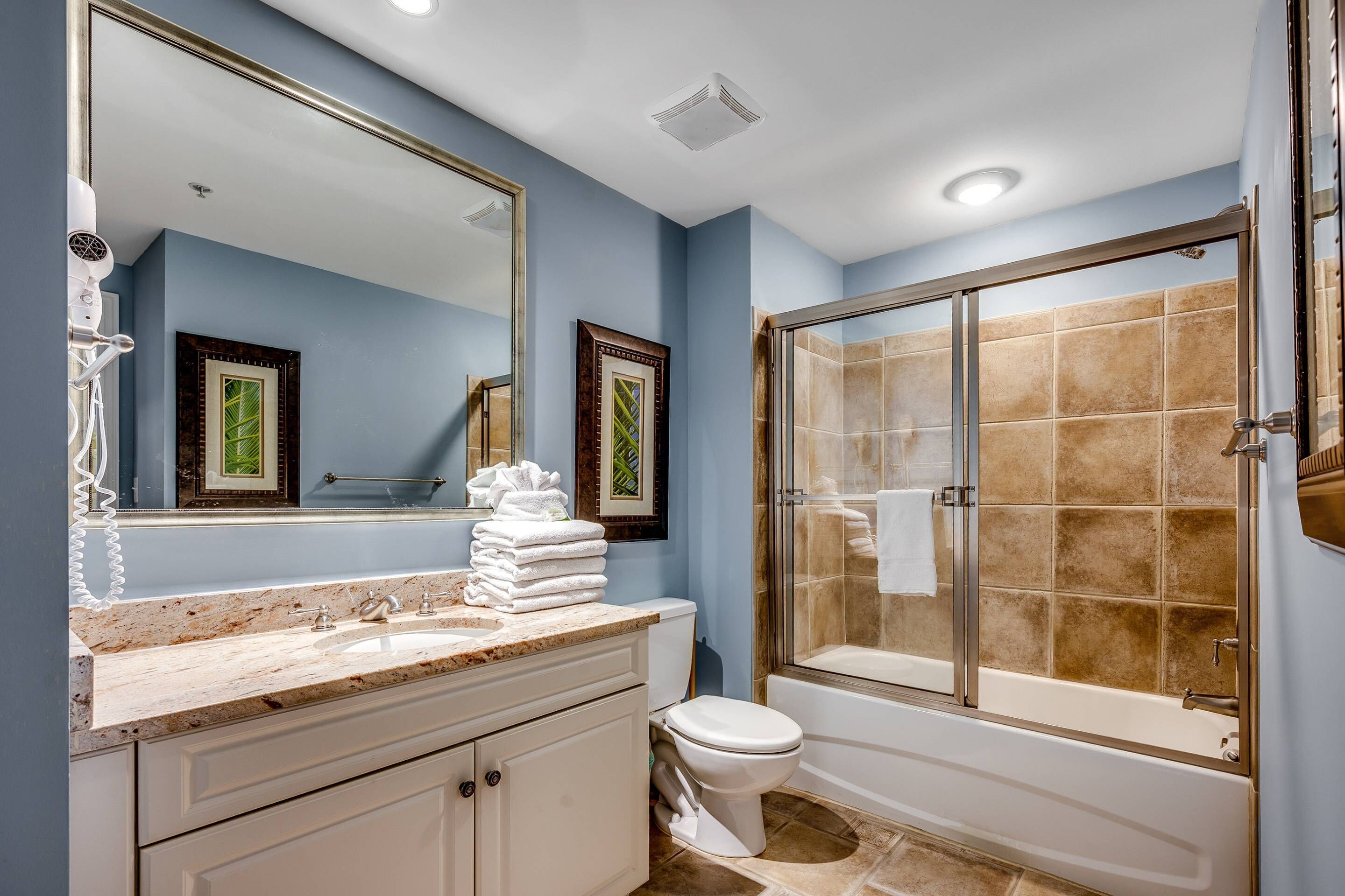 Une salle de bain dotée d’un grand miroir, d’un lavabo, de toilettes et d’une douche à parois de verre.