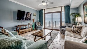 A living room with a flat-screen TV, a ceiling fan, a sofa, a coffee table, and a view of the outdoors through large sliding glass doors.