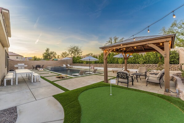 Ein Garten mit Schwimmbad, Terrassenmöbeln, Grill und überdachter Sitzecke.