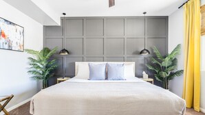 Ein modernes Schlafzimmer mit einem großen Bett, zwei Nachttischen, einem grauen Kopfteil und einem großen, abstrakten Gemälde an der Wand.