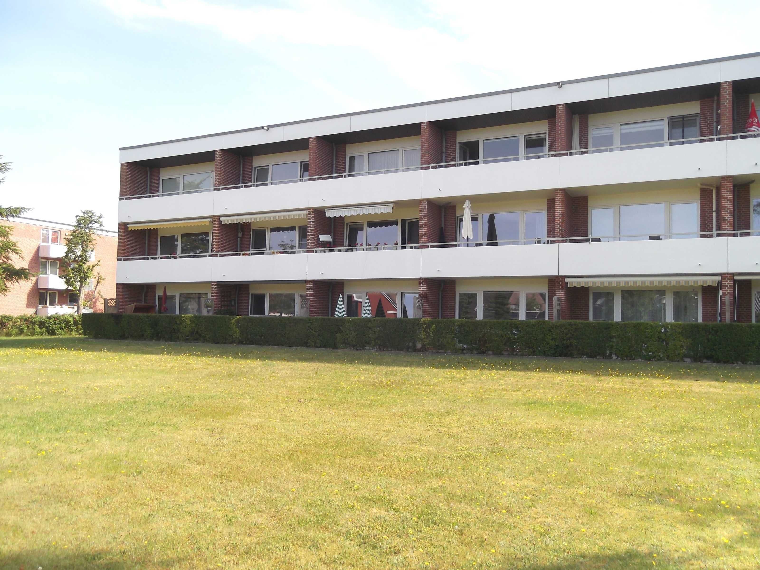 Ein mehrgeschossiges Gebäude mit Flachdach, rechteckigen Fenstern und einem Balkon im oberen Stockwerk.