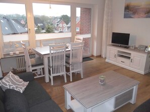Un salon moderne comprenant un canapé, une table à manger, des chaises, un téléviseur et un meuble.