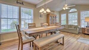 A dining room with a wooden table, benches, and a chandelier. There are large windows with blinds, a ceiling fan, and a wooden cabinet. - 3 Mi to Coast: Pool & Serene Pond Views (Ocean View)