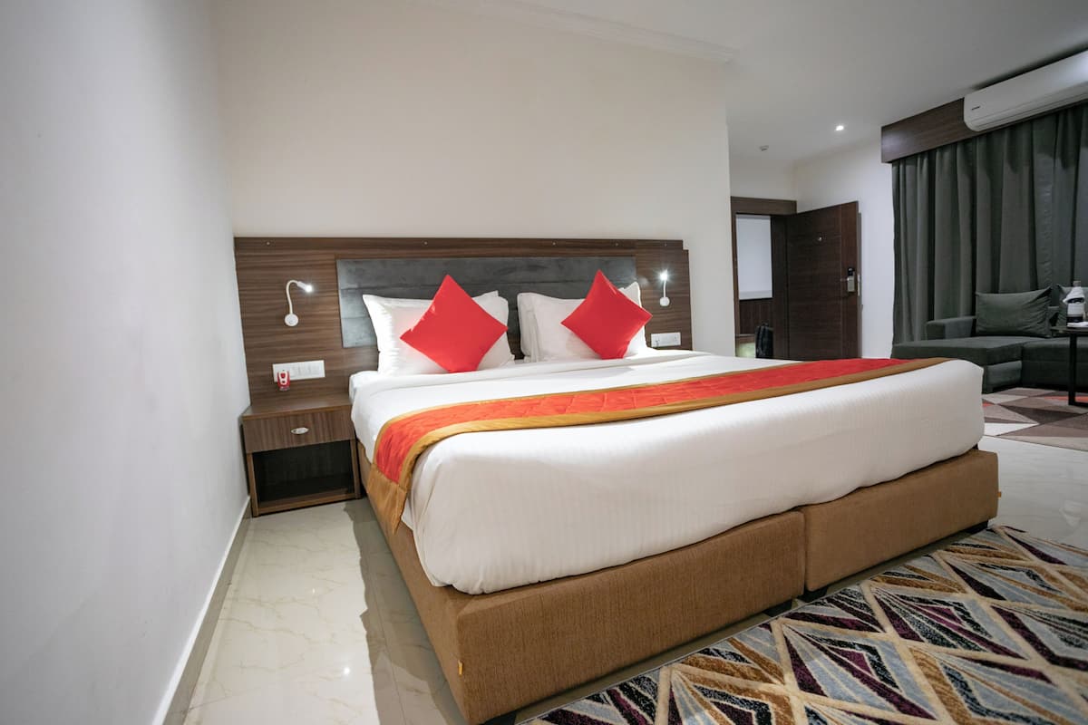 Quarto de hotel com uma cama grande, uma mesa de cabeceira, um sofá e um tapete estampado.