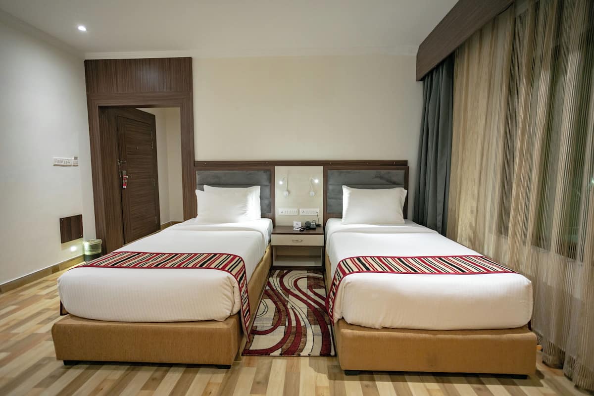 Quarto de hotel com duas camas, uma cabeceira de madeira, uma mesa de cabeceira e uma janela com cortinas.