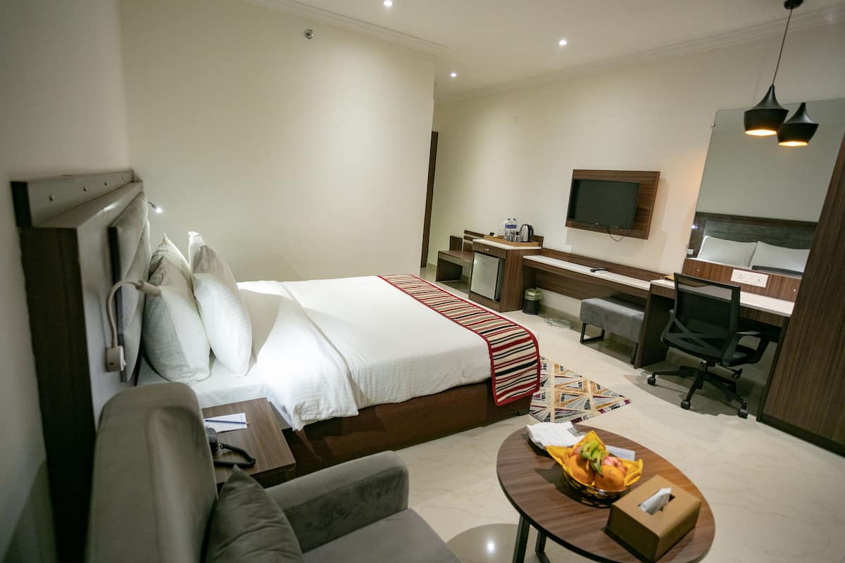 Quarto de hotel com uma cama, uma escrivaninha, uma cadeira, uma televisão e uma mesinha com fruta.