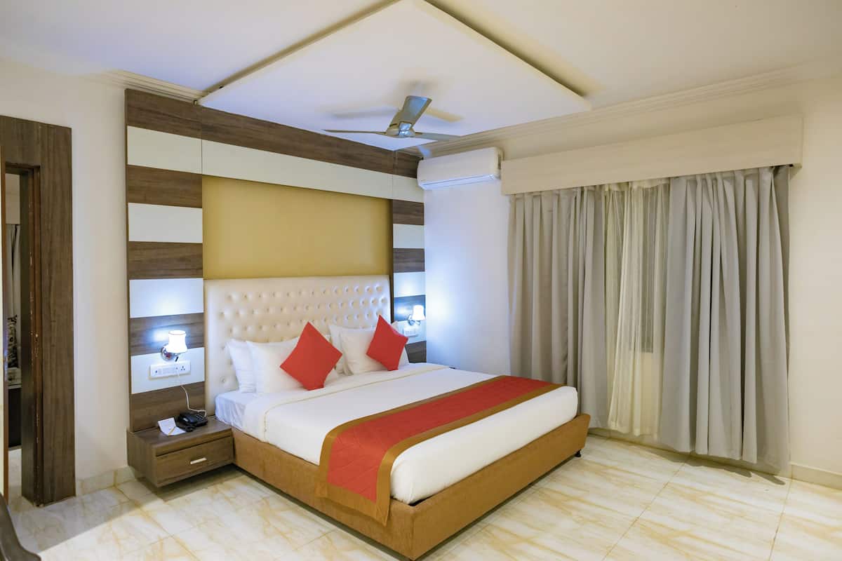 Quarto de hotel com uma cama grande, um ventilador de teto, mesa de cabeceira com telefone e janela com cortinas.