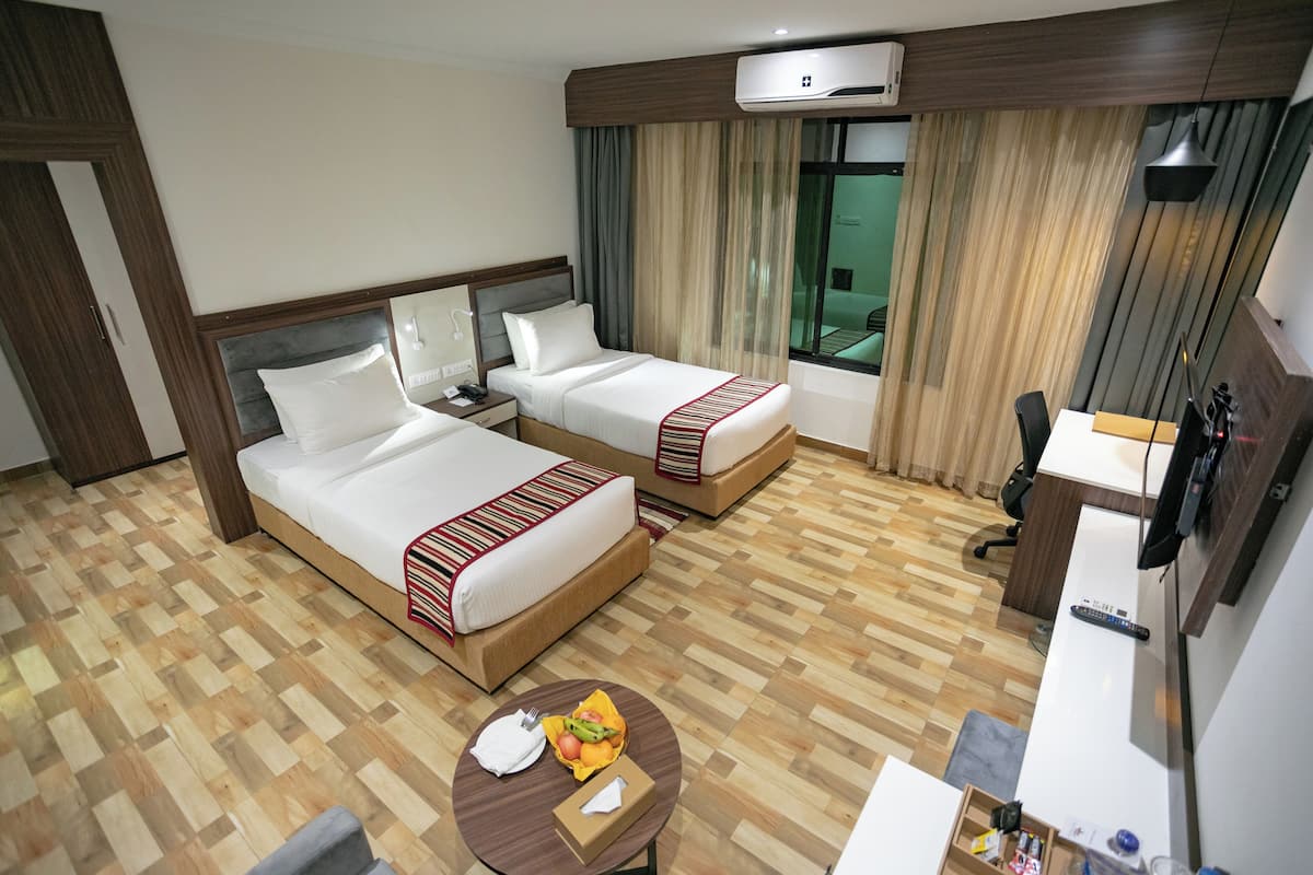 Quarto de hotel com duas camas, uma escrivaninha, uma cadeira, uma mesa pequena com uma fruteira e uma televisão.