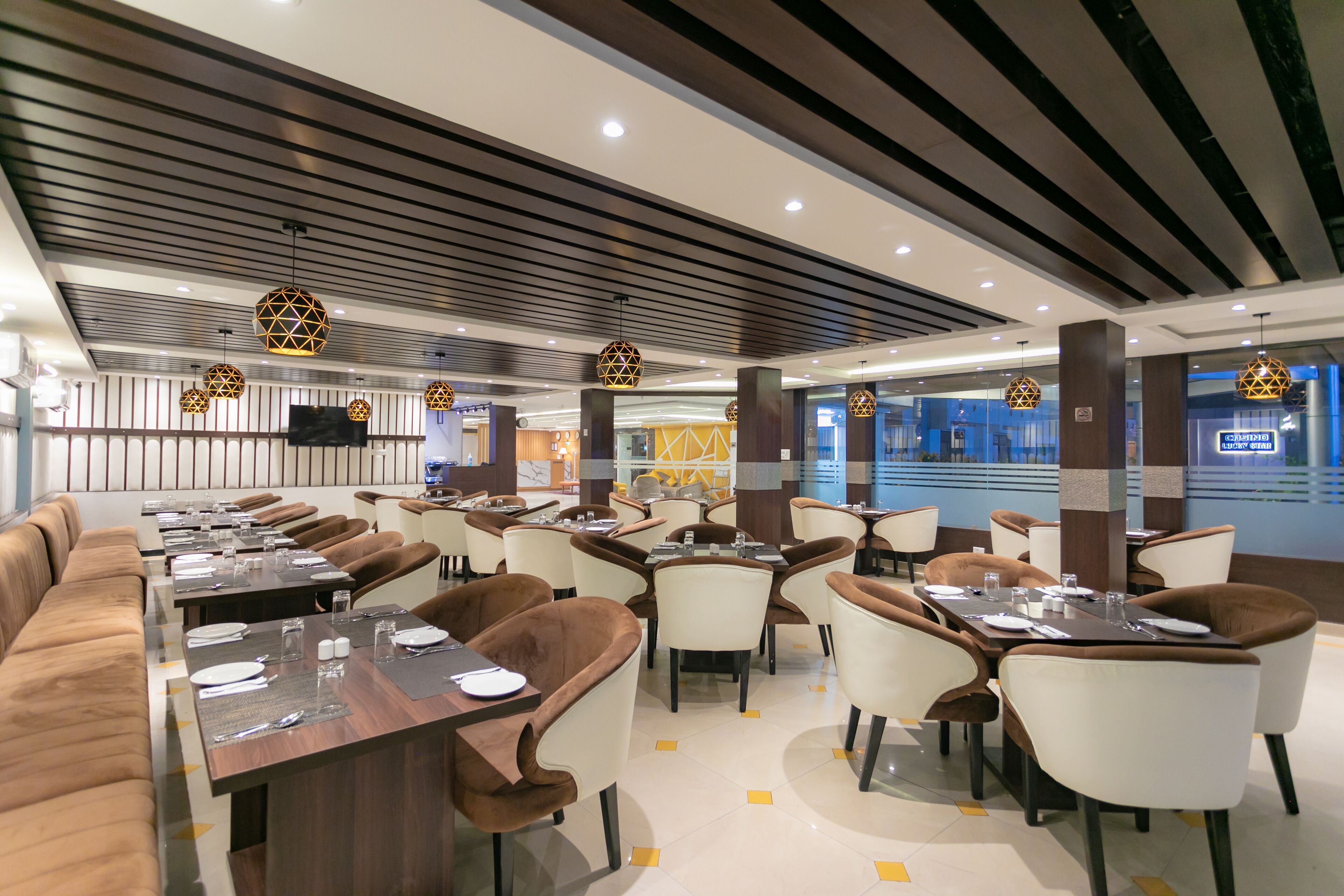 A modern dining area with long tables and cushioned seating, featuring geometric pendant lighting and a clean, contemporary design.