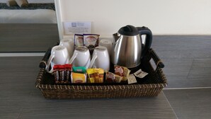 Un panier en osier contenant une tasse de la gamme Nescafe Blend 3, une tasse de la gamme Nescafe Blend 4, un sachet de thé Lipton, un paquet de biscuits et une cafetière Maxim en argent.