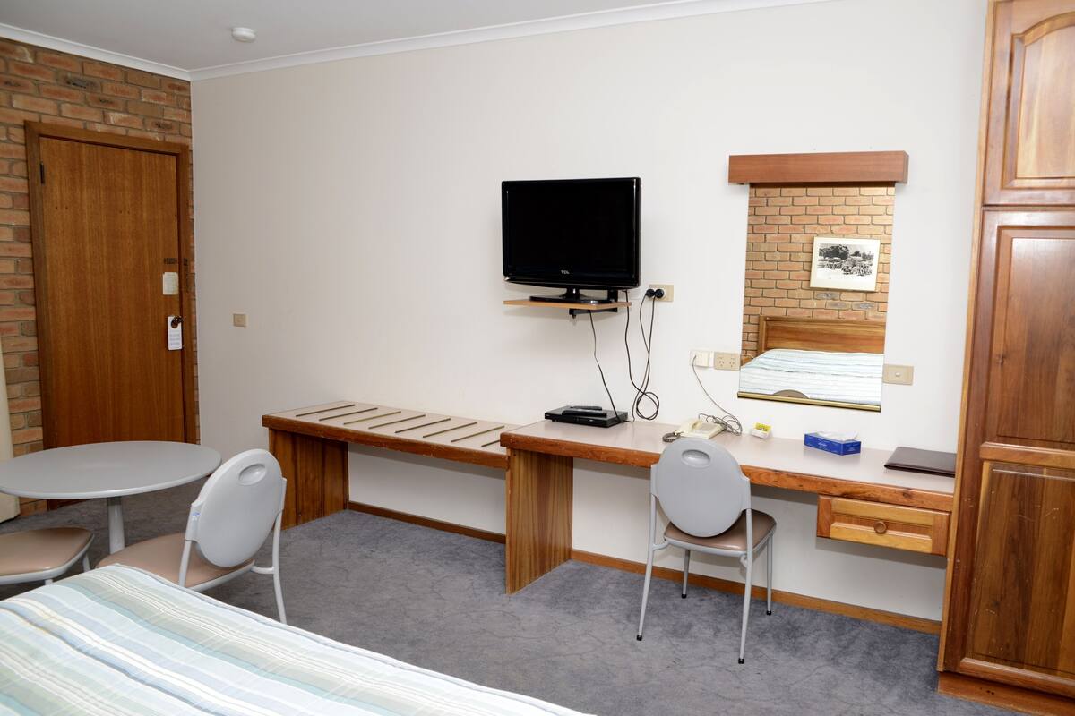 Une chambre d’hôtel comprenant un lit, un bureau avec un ordinateur, une télévision, une chaise et une armoire.