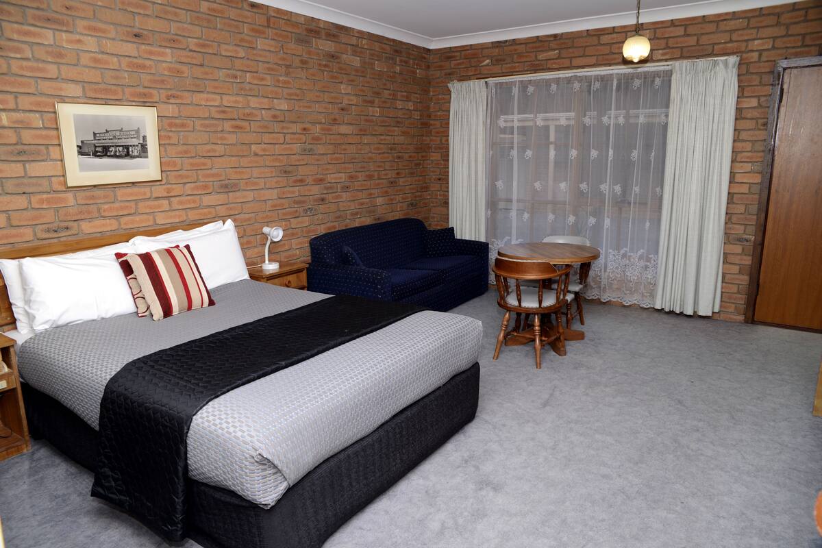 Une chambre d’hôtel avec un mur en briques, un lit recouvert d’une courtepointe noire et blanche, un canapé bleu, une petite table en bois et une chaise.