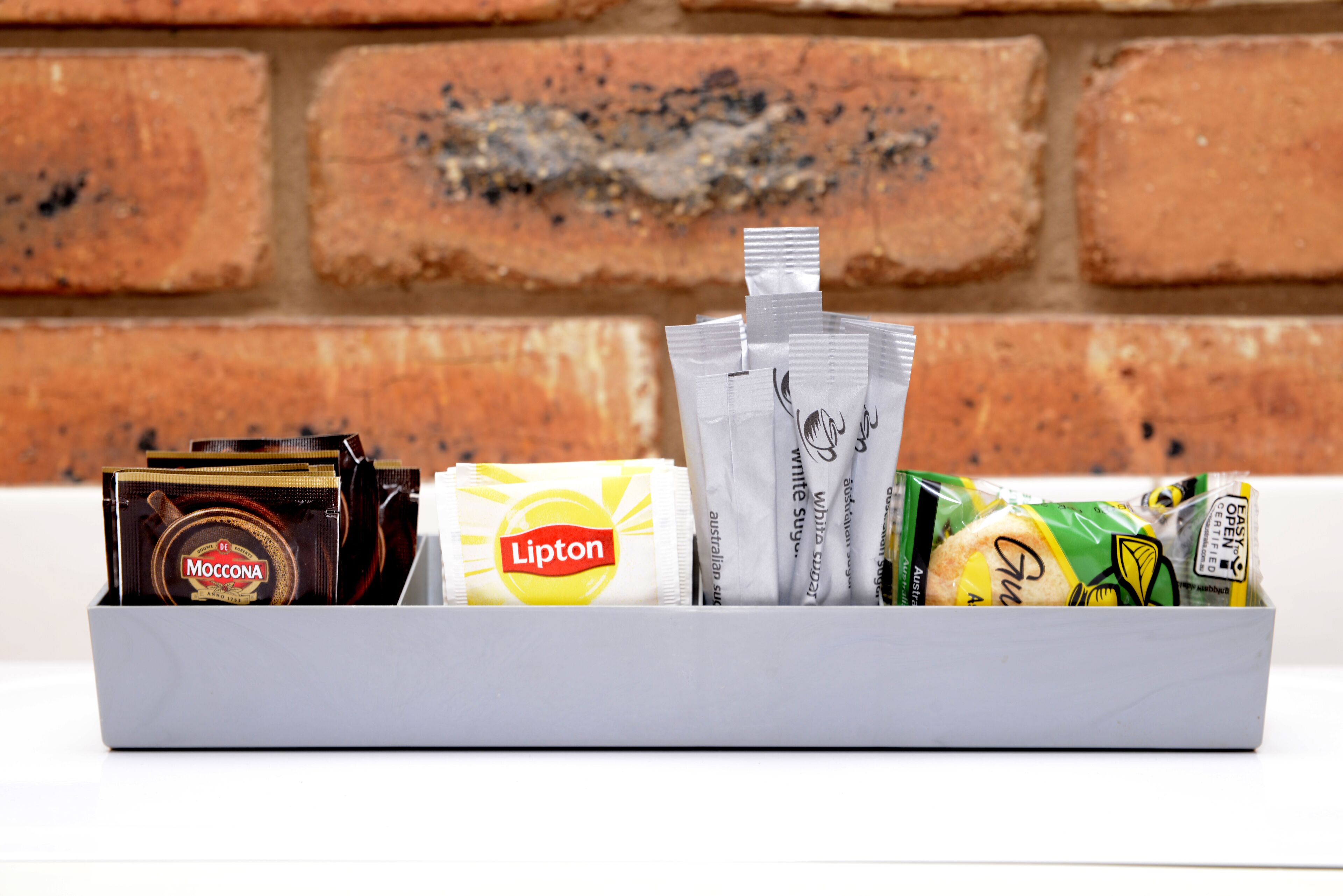 A tray with various packaged food items including Lipton tea, Moccona coffee, and other snacks.