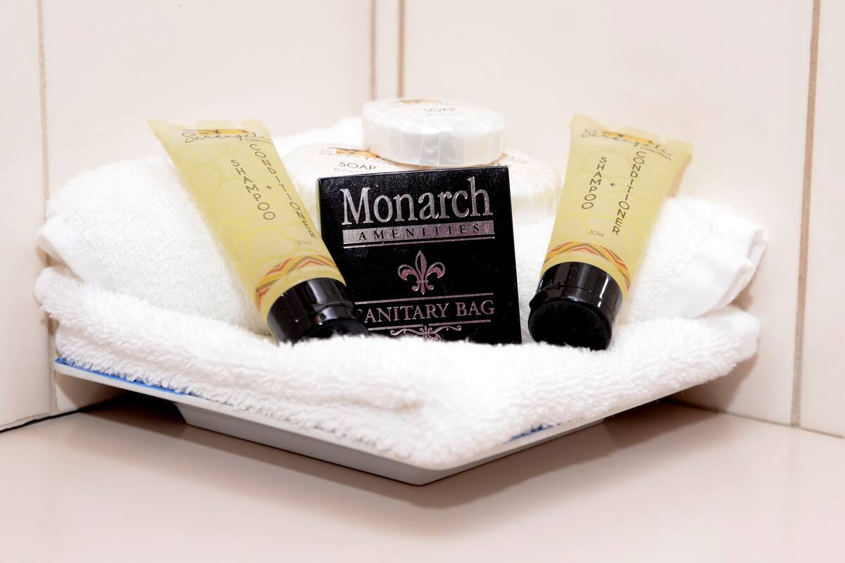 Un coin lavabo dans la salle de bain, avec une serviette blanche, un sac hygiénique de la marque Monarch et deux tubes de shampoing.