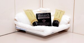 A bathroom sink area with a white towel, a Monarch sanitary bag, and two shampoo tubes.