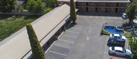 Vista aérea de un estacionamiento con piscina, varios autos y un edificio de techo plano.