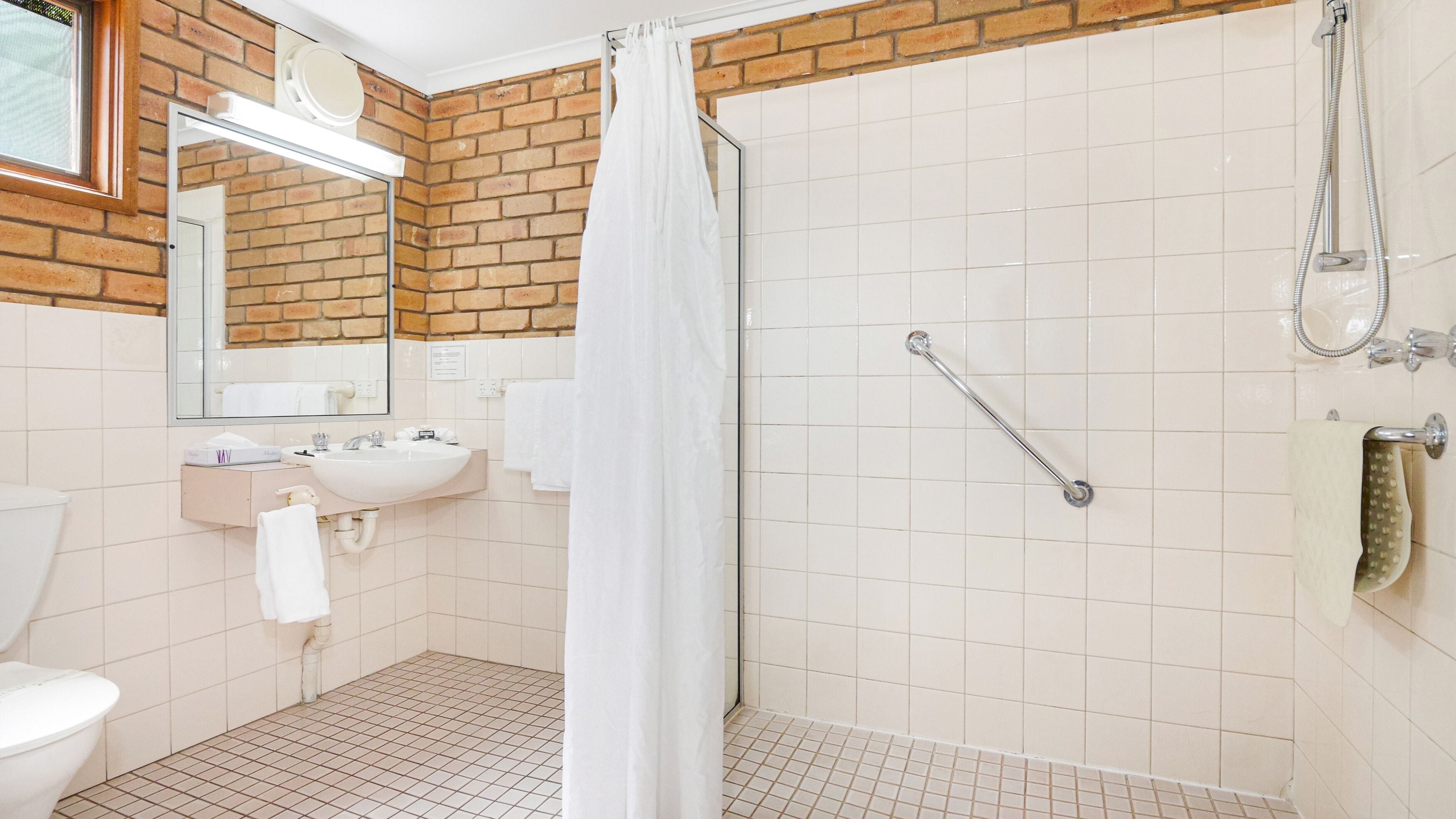 A bathroom with a shower, toilet, sink, and a mirror.