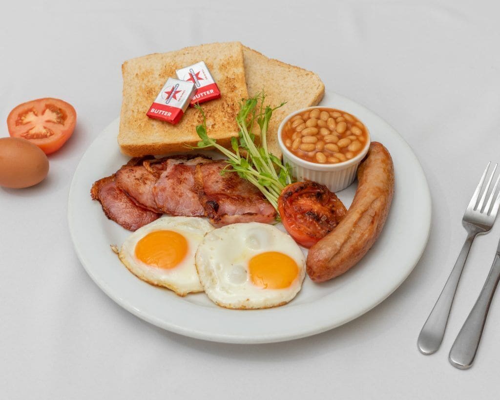 A plate with bacon, sausages, eggs, toast, beans, and a tomato.