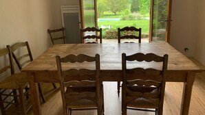 Un coin repas avec une table et des chaises en bois, donnant sur un jardin grâce à des portes vitrées.