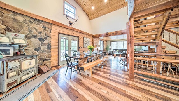 A rustic interior with a stone wall, wooden ceiling, and a dining area with benches and a table.